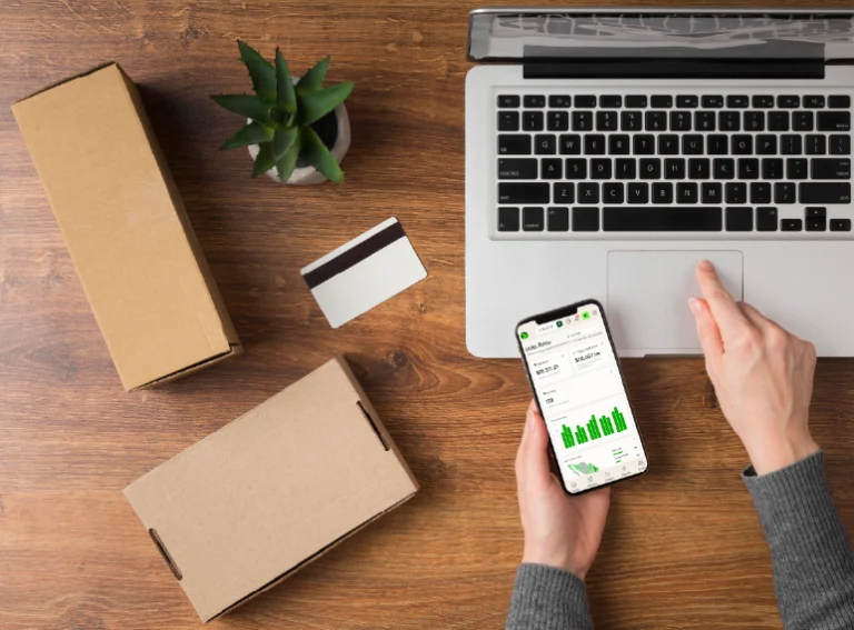 Escritorio con laptop, smartphone con gráficas, tarjetas y paquetes de envío.