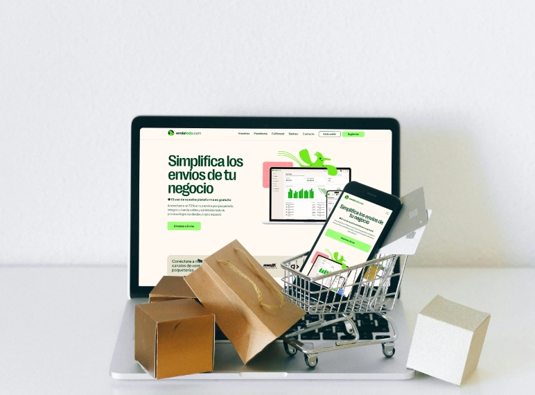 Vista de una laptop y un smartphone mostrando la plataforma de gestión de envíos de EnviaTodo.com. Frente a ellos, hay varias cajas de cartón de e-commerce y un carrito de compras de juguete lleno de paquetes, simbolizando la logística de ventas online simplificada
