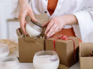 persona empaquetando unas velas aromanicas para un envio. Las velas son blancas en un vaso de vidrio