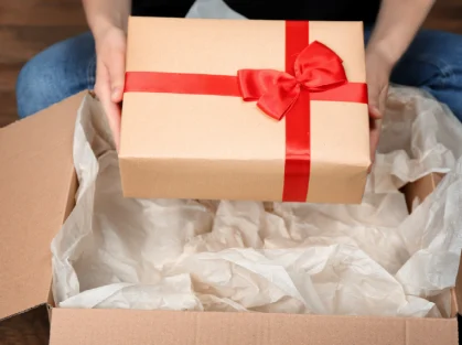Manos abriendo una caja de cartón con un lazo rojo y papel de seda.