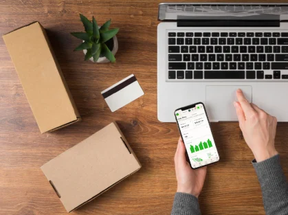 Escritorio con laptop, smartphone con gráficas, tarjetas y paquetes de envío.